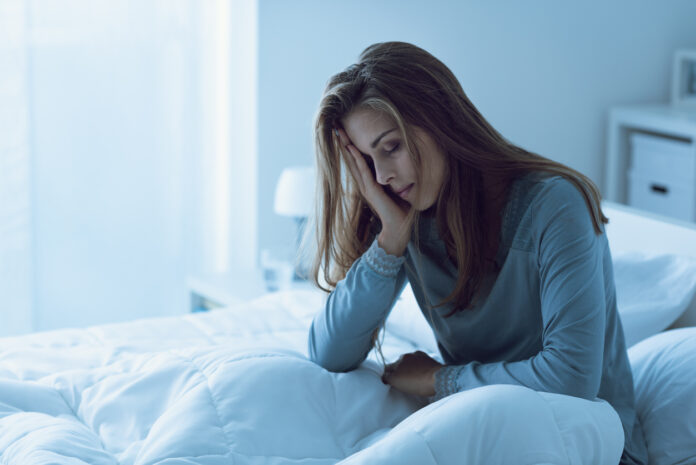 Depressed woman awake in the night, she is touching her forehead and suffering from insomnia