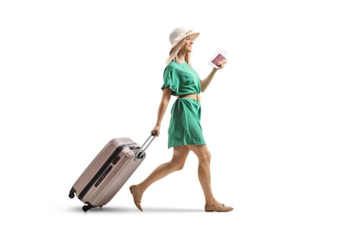 Young woman in a green dress pulling a suitcase and holding a passport