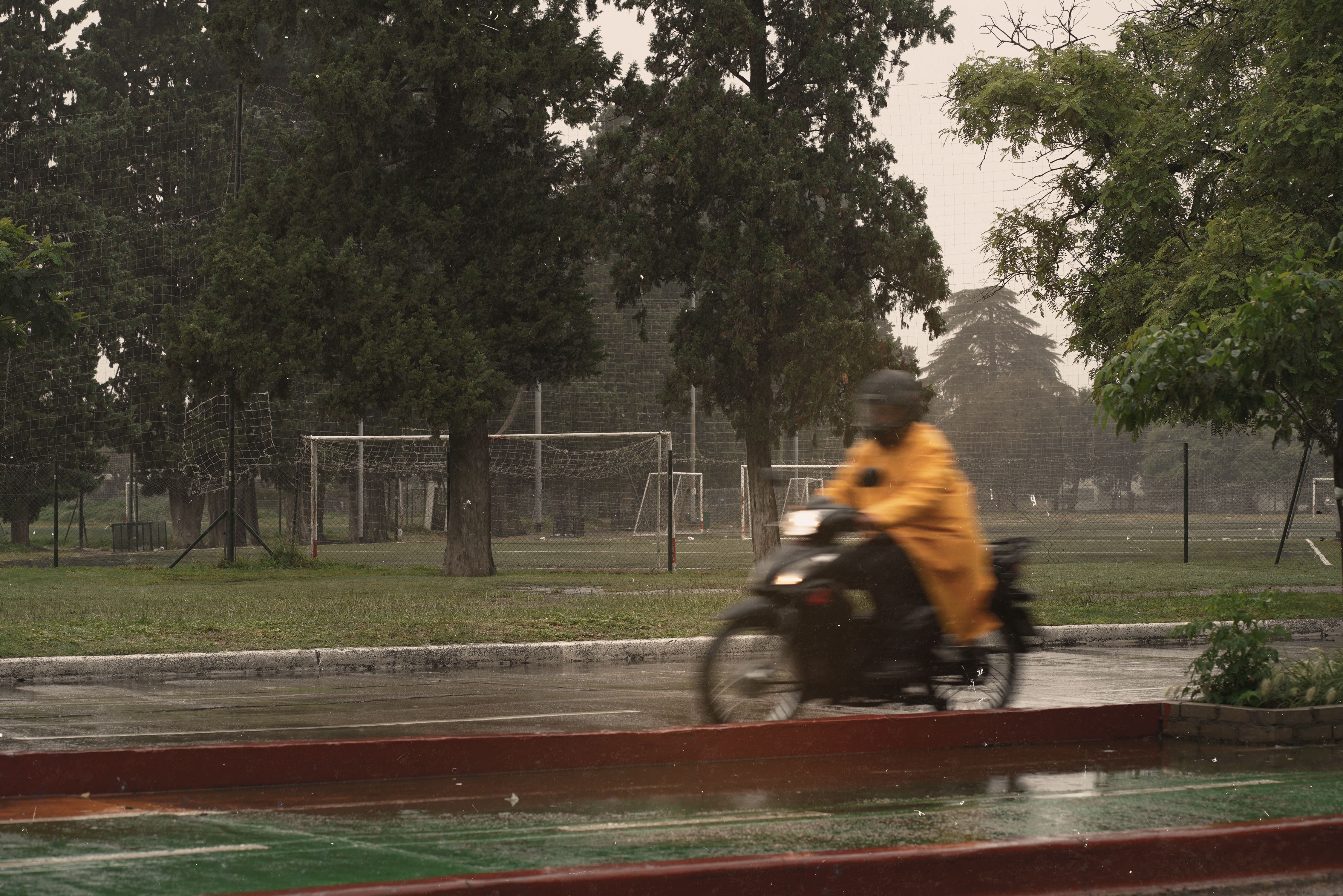 Motorbike rider in a yellow waterproof suit riding through the rain in a park