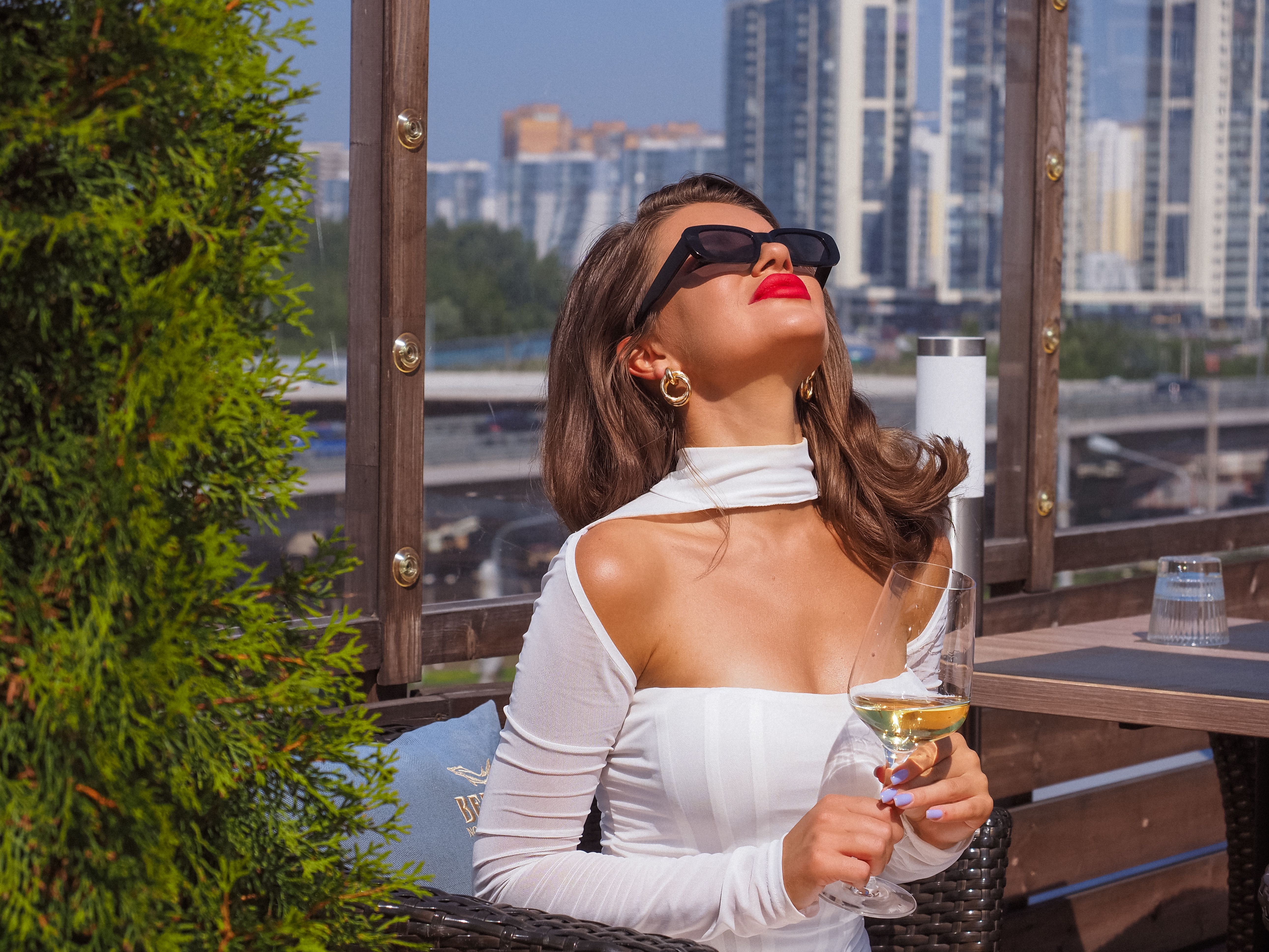 A stylish woman relaxing with a wine glass on a city rooftop, evoking a premium lifestyle experience